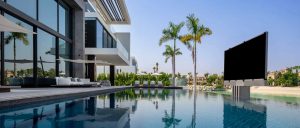 Luxury pool with large screen TV in it and palm trees in the background.