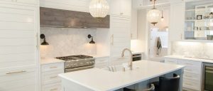 White kitchen with 2 chandeliers, island, 2 bar stool, white panel cabinets.