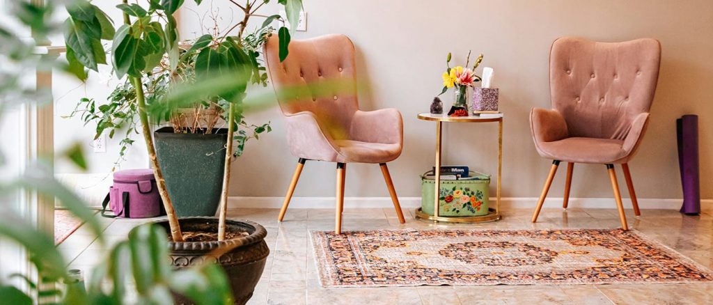 plants by a window, 2 peach colored chairs with a small table in the middle candles and plants. peach with pattern rug in front.