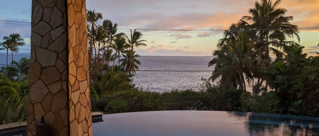 View from a pool with trees of the ocean at sunset.